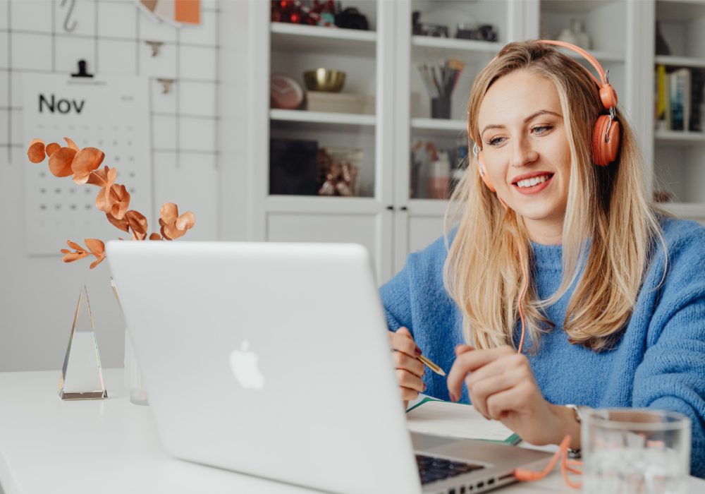 "woman sitting in her home office by her desk looking at her open mac laptop